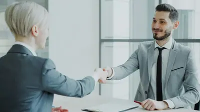 Two people shaking hands across a desk after a meeting